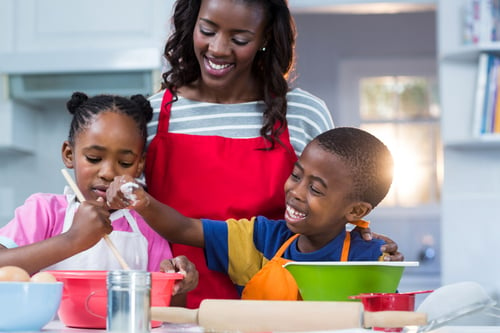 Children preparing cake with their mother in kitchen