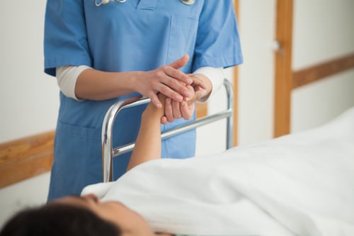 Patient lying on a medical bed holding the hand of a nurse in hospital corridor